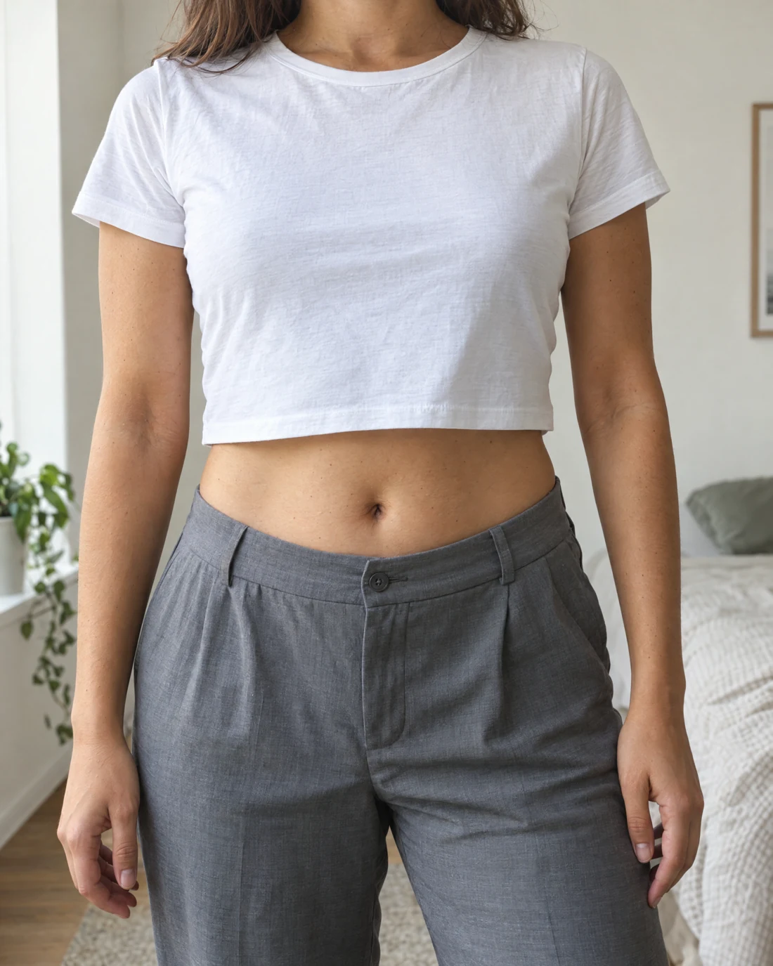 Femme en crop top blanc et pantalon gris, ventre visible de face