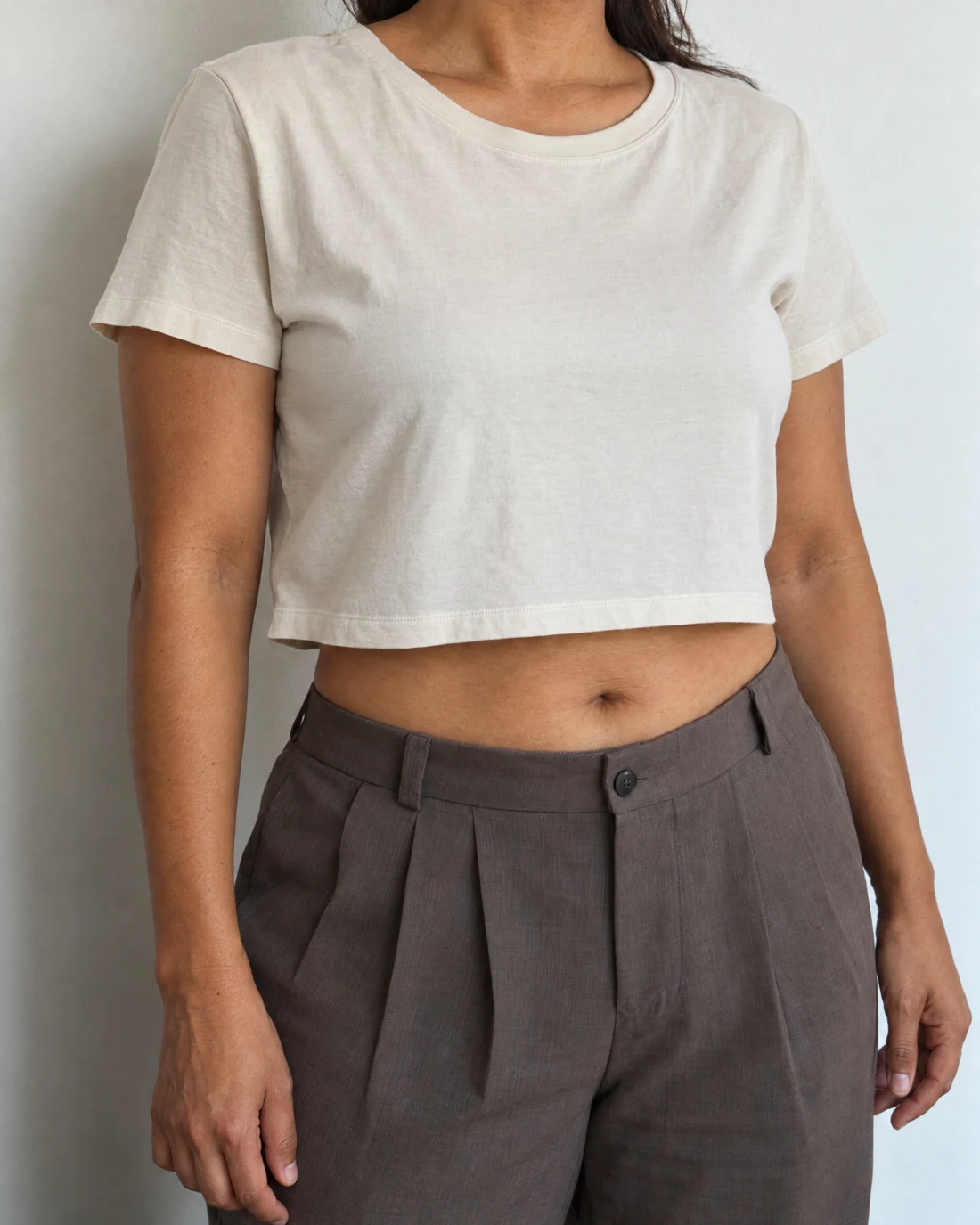 Femme en crop top écru et pantalon taupe, ventre visible de trois quarts